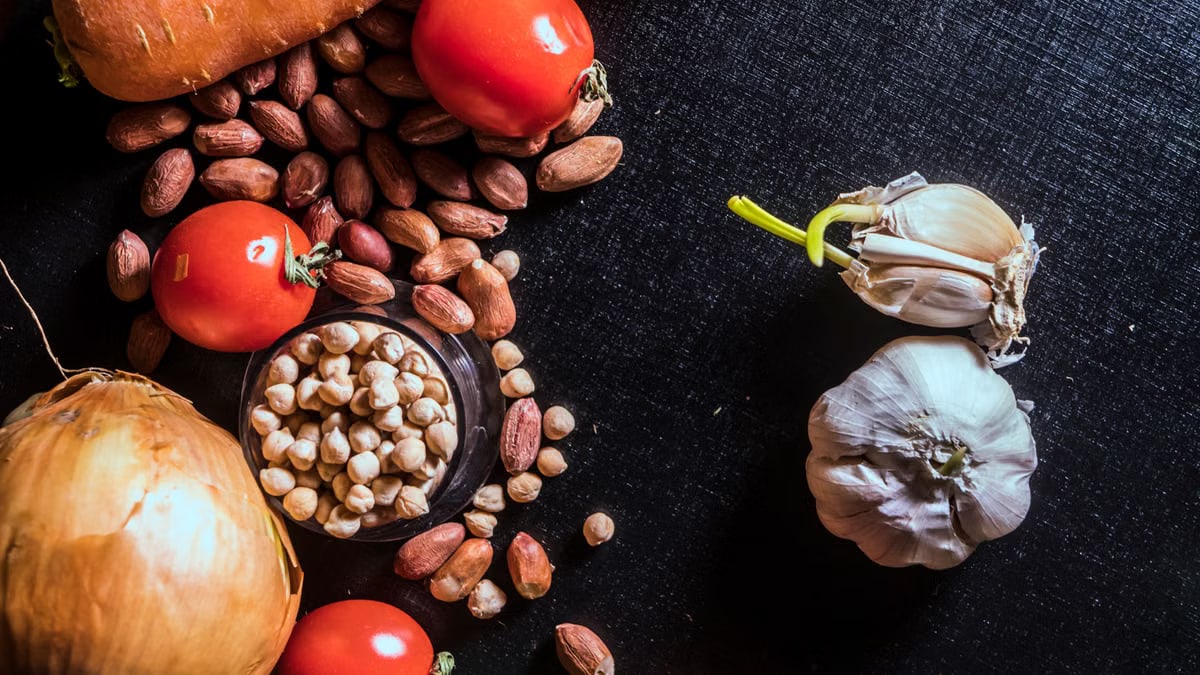 Top view of fresh vegetables and nuts arranged on a dark surface, showcasing raw ingredients.